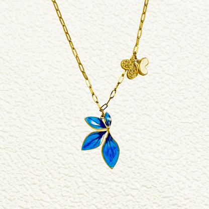 Gold charm necklace with blue enamel leaf, butterfly, and heart on waterproof paperclip chain