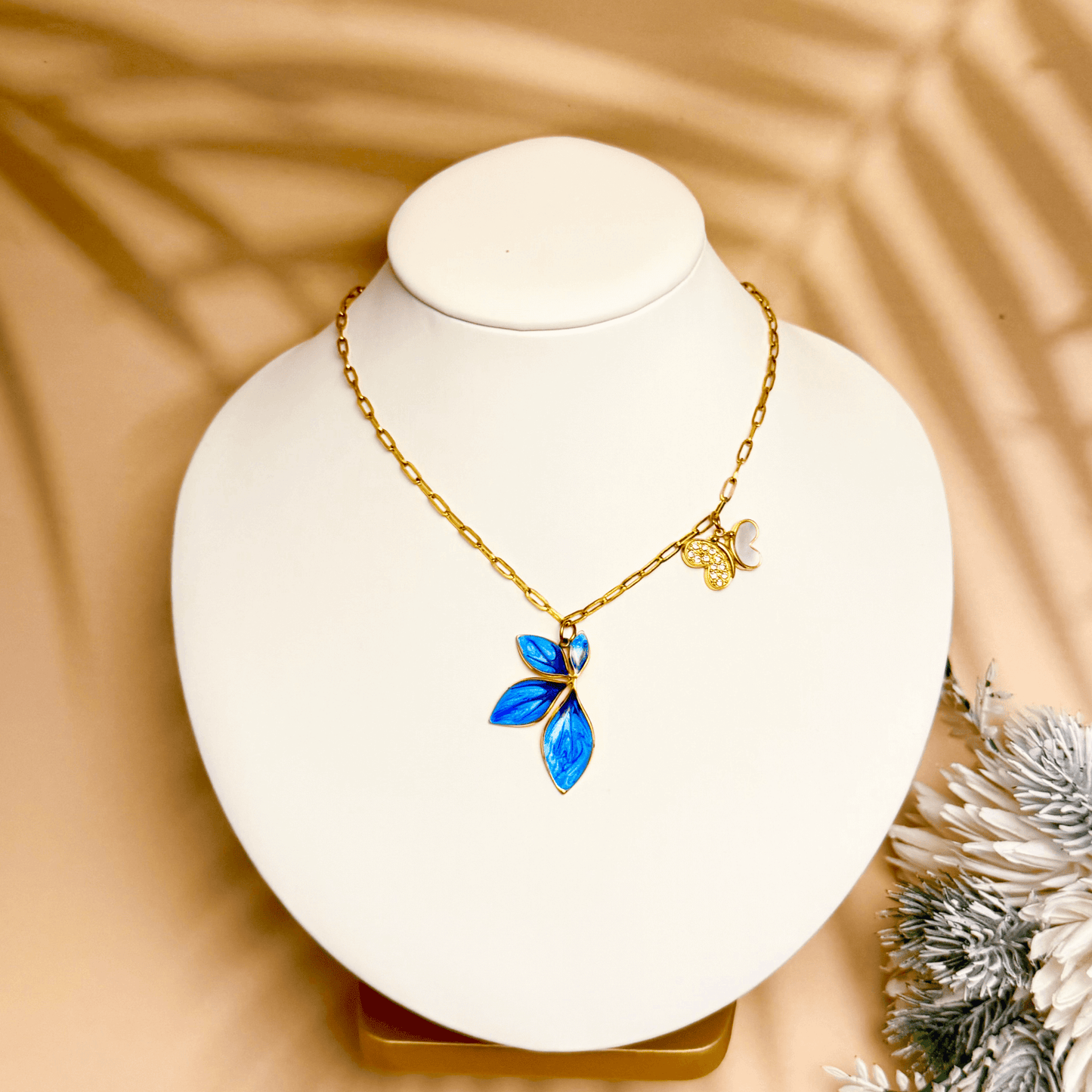 Gold charm necklace with blue enamel leaf, butterfly, and heart on waterproof paperclip chain