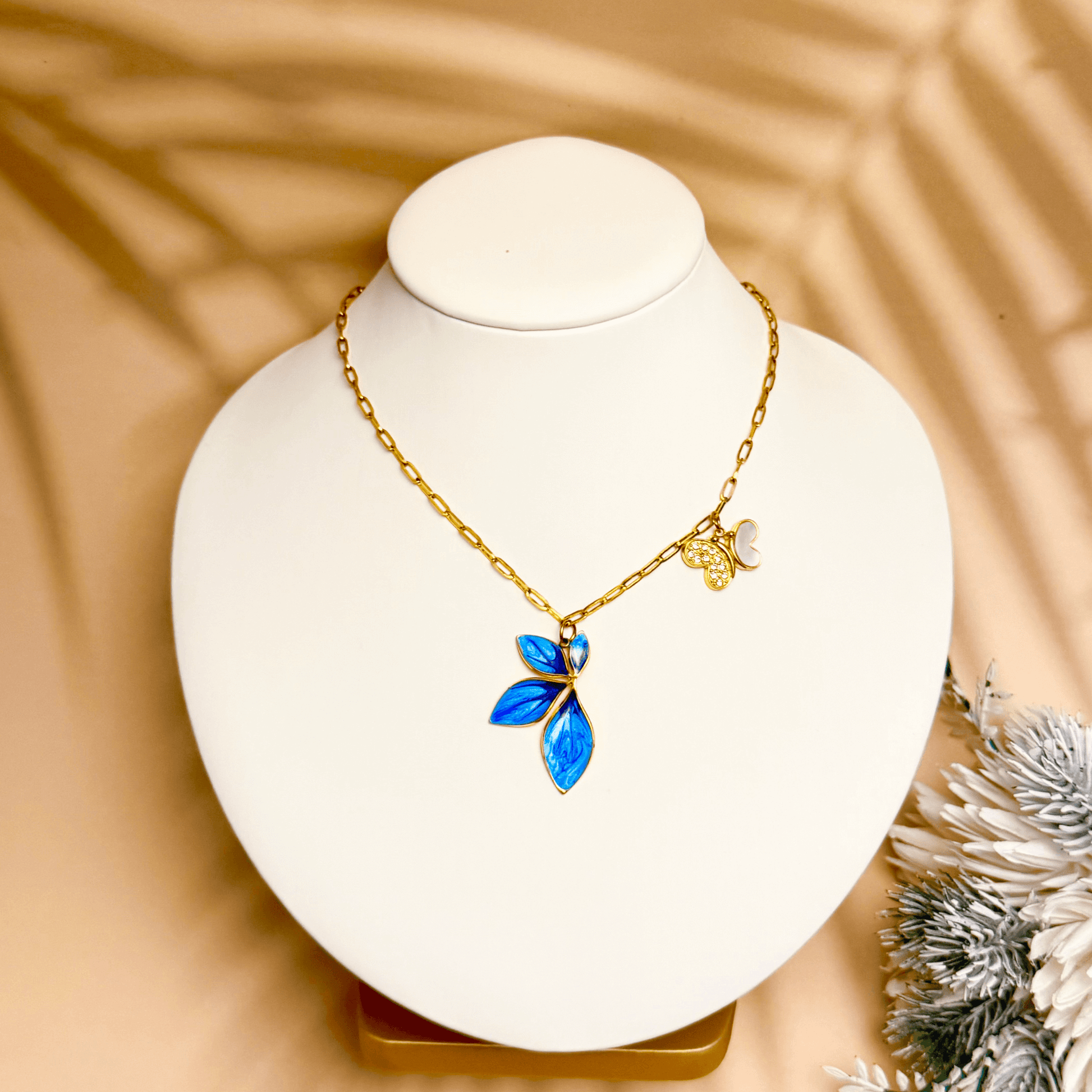 Gold charm necklace with blue enamel leaf, butterfly, and heart on waterproof paperclip chain
