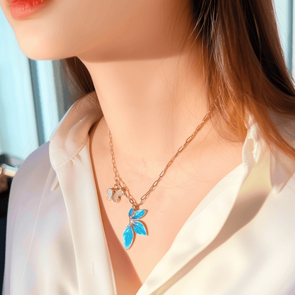 Gold charm necklace with blue enamel leaf, butterfly, and heart on waterproof paperclip chain
