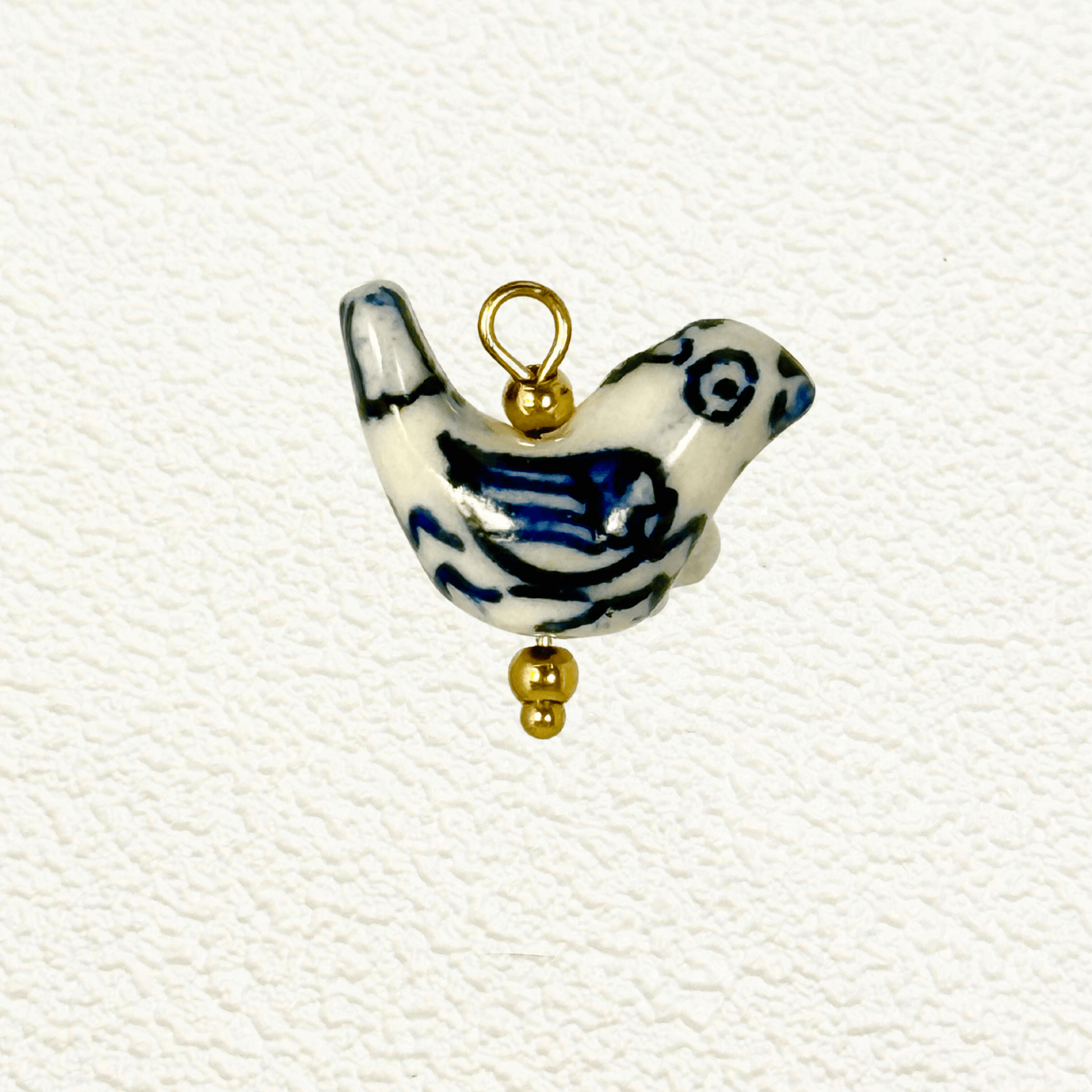 Hand-painted white ceramic charm in the shape of a bird with blue wing detailing and gold beads