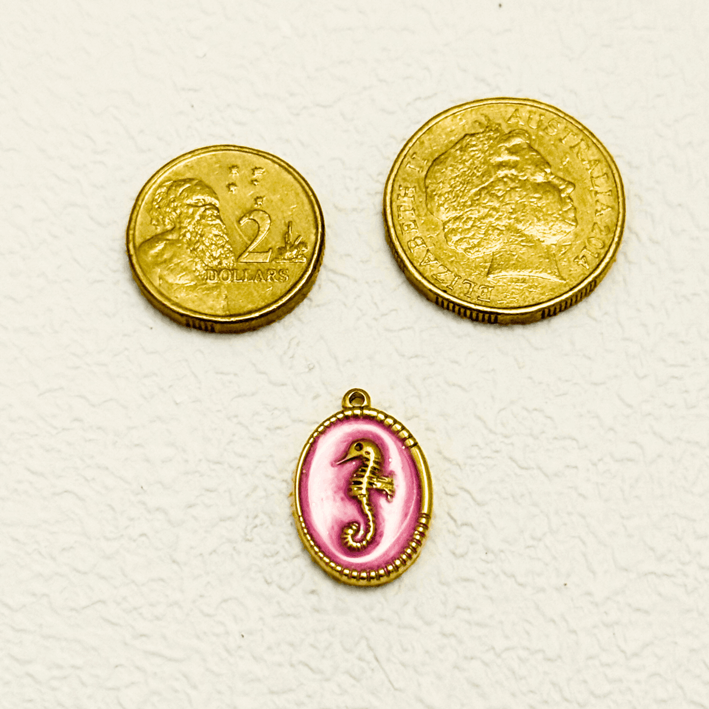 Gold seahorse charm set in an oval medallion with a soft blush pink enamel background and detailed golden beaded edge.