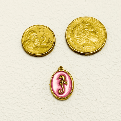 Gold seahorse charm set in an oval medallion with a soft blush pink enamel background and detailed golden beaded edge.