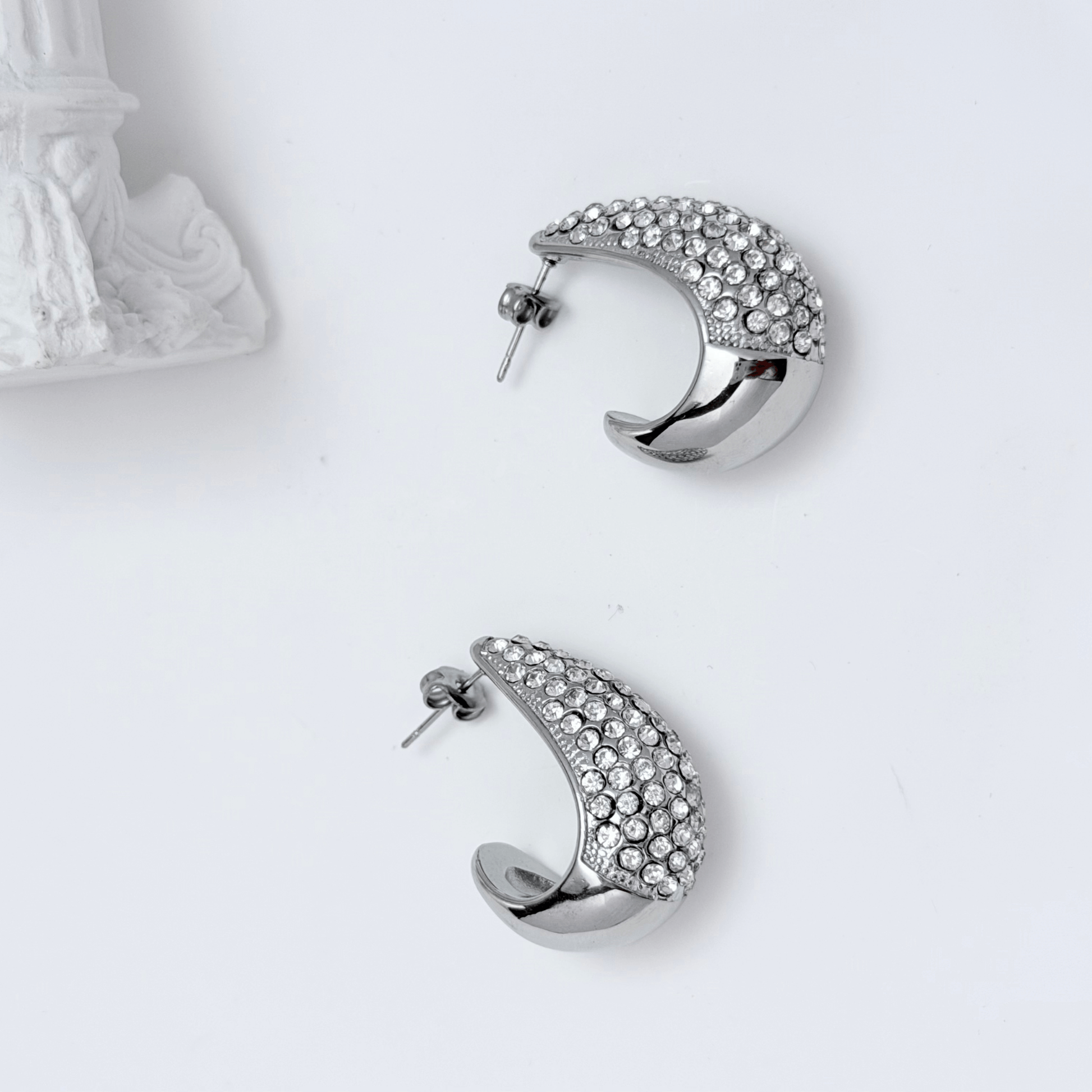 Chunky pavé silver half hoop earrings with crystal detailing, photographed on a light background.