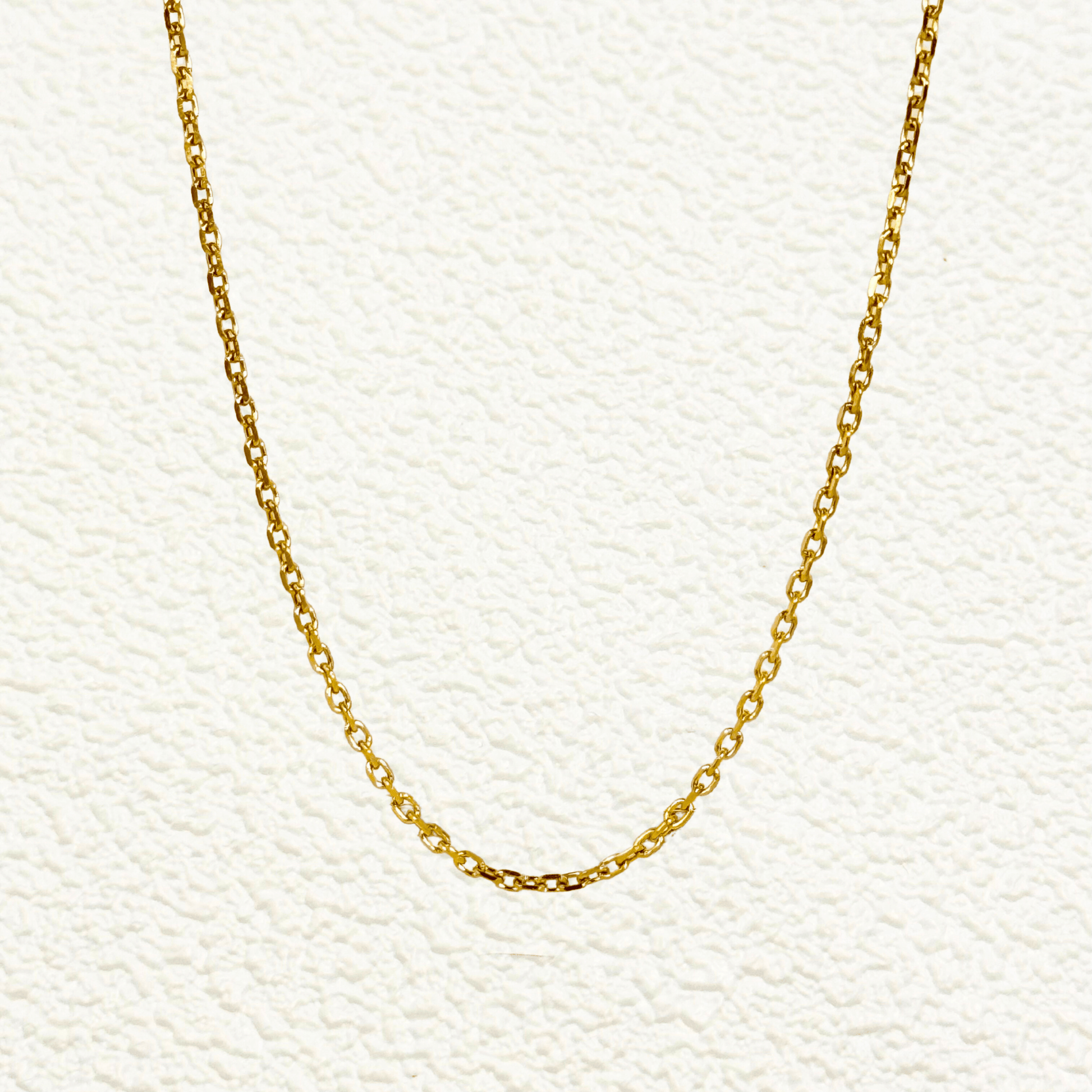 Gold cable chain made of fine interlocking links in a classic minimalist style, available as necklace, bracelet, or anklet