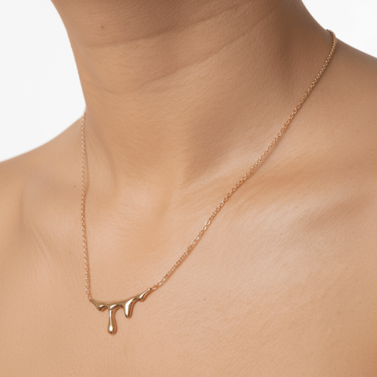 Gold drip-style pendant necklace with a sleek molten design on a fine chain, displayed on a white bust with soft floral accents.