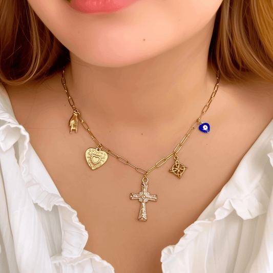 Gold charm necklace with cross, evil eye, sacred heart, hamsa hand, and Celtic knot on paperclip chain