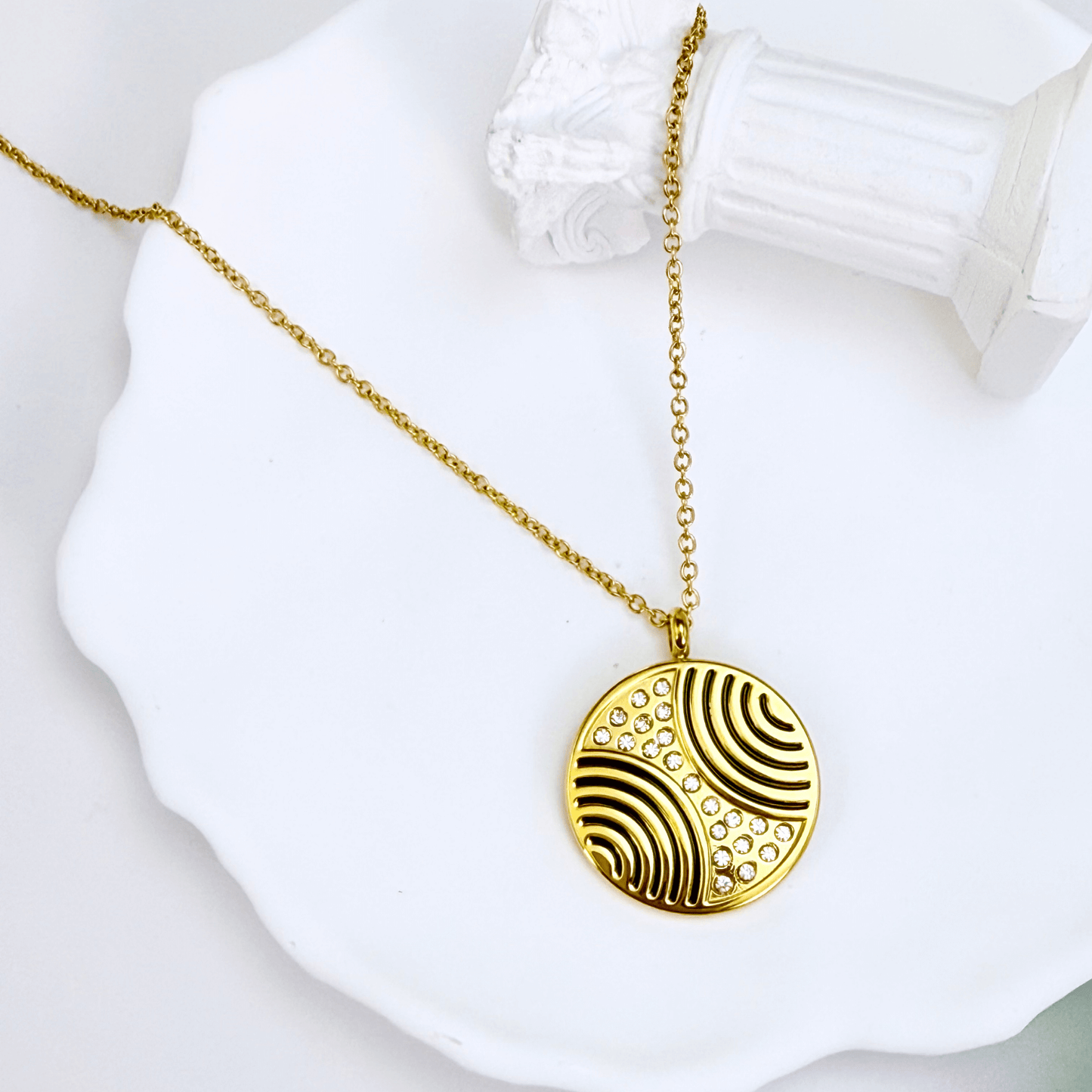 Gold round pendant necklace with engraved flowing pattern and crystal detailing, symbolising harmony and balance.