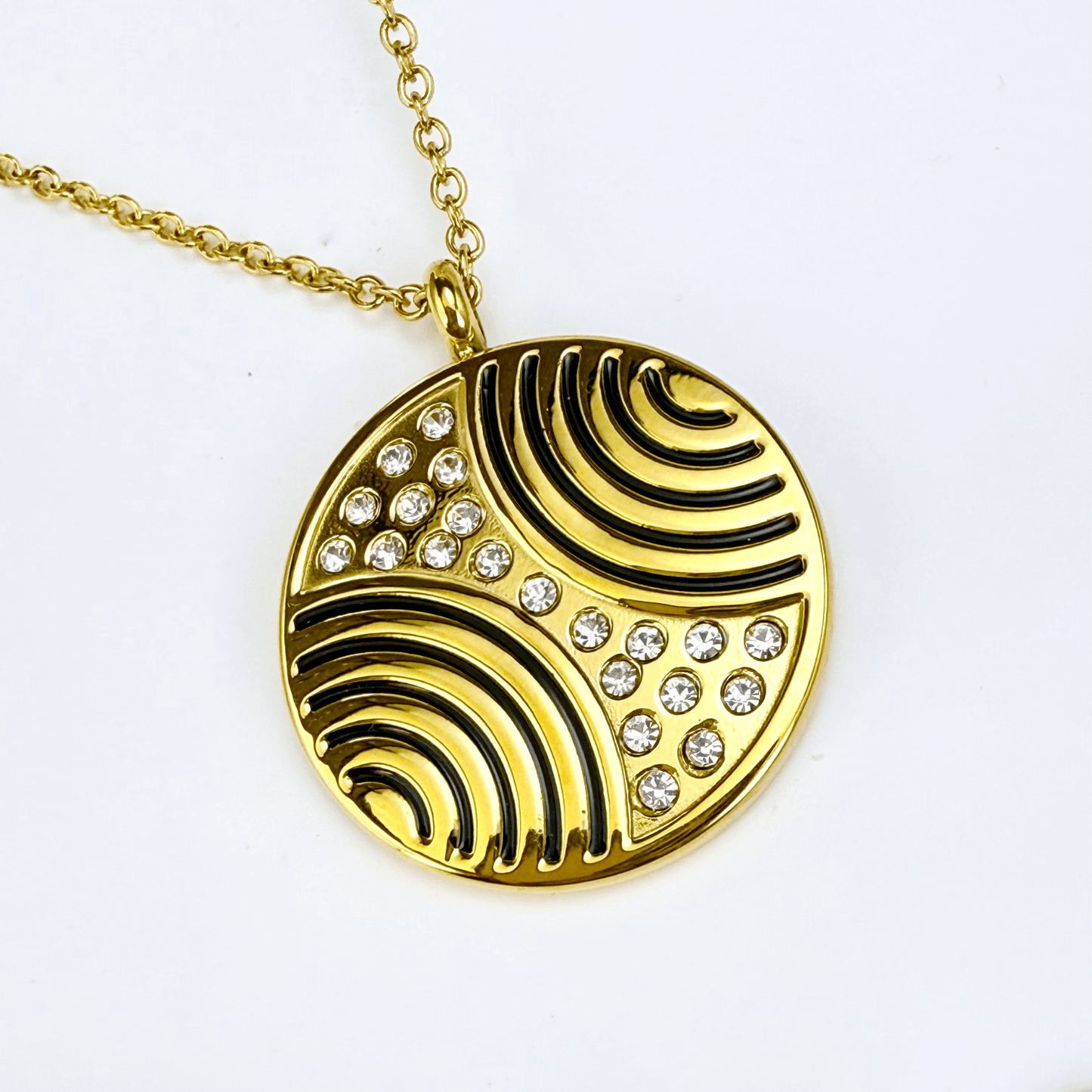 Gold round pendant necklace with engraved flowing pattern and crystal detailing, symbolising harmony and balance.