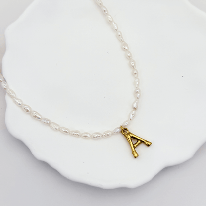 A delicate necklace made of irregular white keshi pearls featuring a gold-toned textured initial pendant in the shape of the letter A.