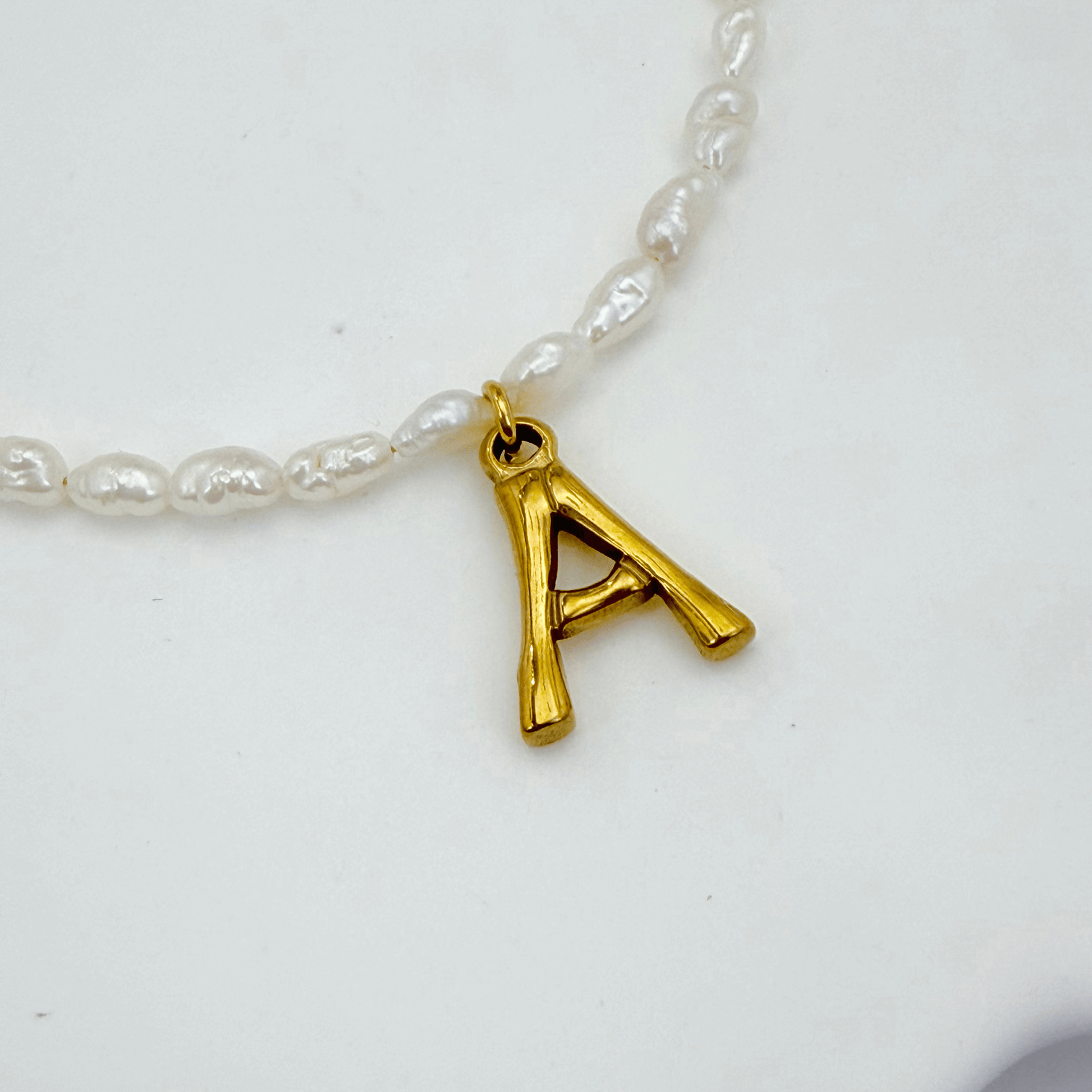 A delicate necklace made of irregular white keshi pearls featuring a gold-toned textured initial pendant in the shape of the letter A.