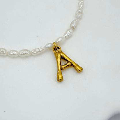 A delicate necklace made of irregular white keshi pearls featuring a gold-toned textured initial pendant in the shape of the letter A.