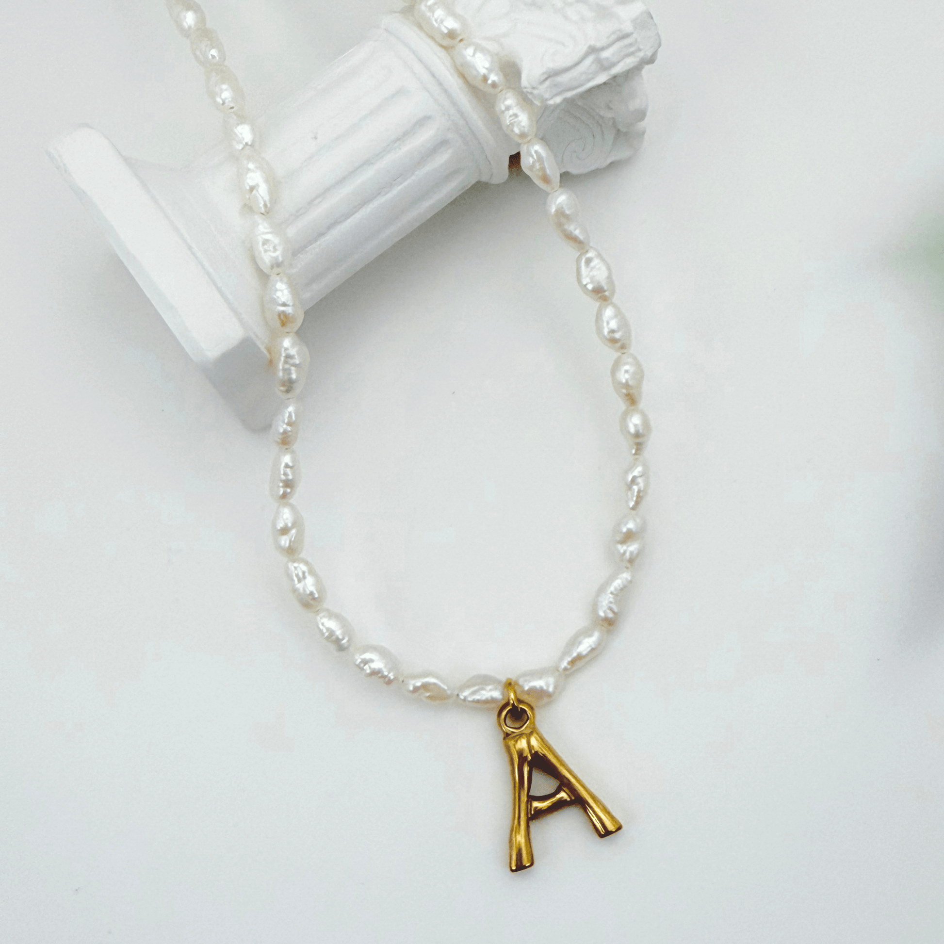 A delicate necklace made of irregular white keshi pearls featuring a gold-toned textured initial pendant in the shape of the letter A.