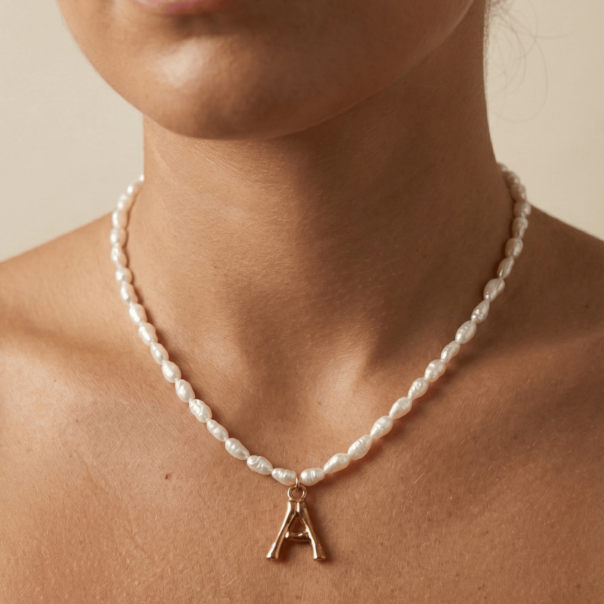 A delicate necklace made of irregular white keshi pearls featuring a gold-toned textured initial pendant in the shape of the letter A.