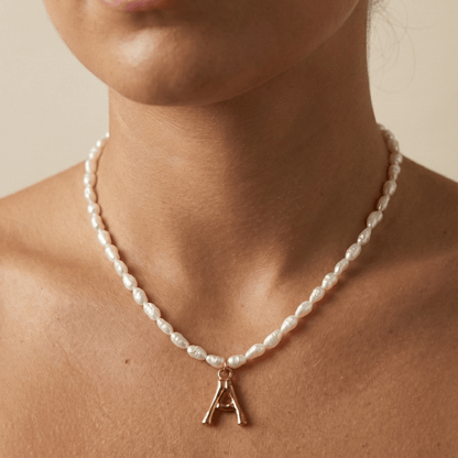 A delicate necklace made of irregular white keshi pearls featuring a gold-toned textured initial pendant in the shape of the letter A.