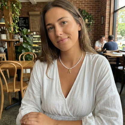 A delicate necklace made of irregular white keshi pearls featuring a gold-toned textured initial pendant in the shape of the letter A.