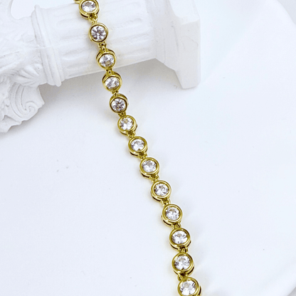Gold crystal tennis bracelet with bezel-set clear stones.