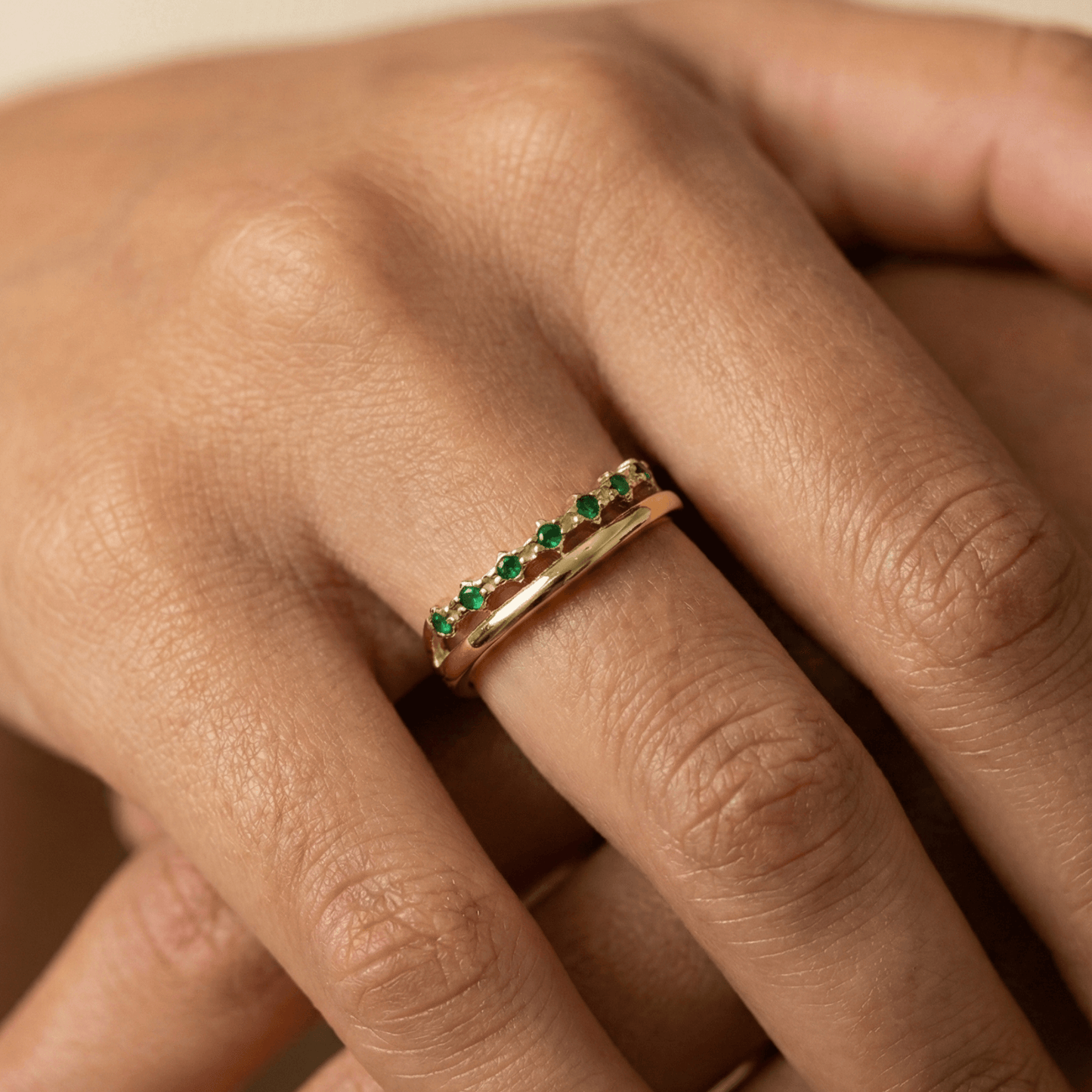 Gold curved stacking ring with emerald green crystals on white pedestal MXW Jewellery