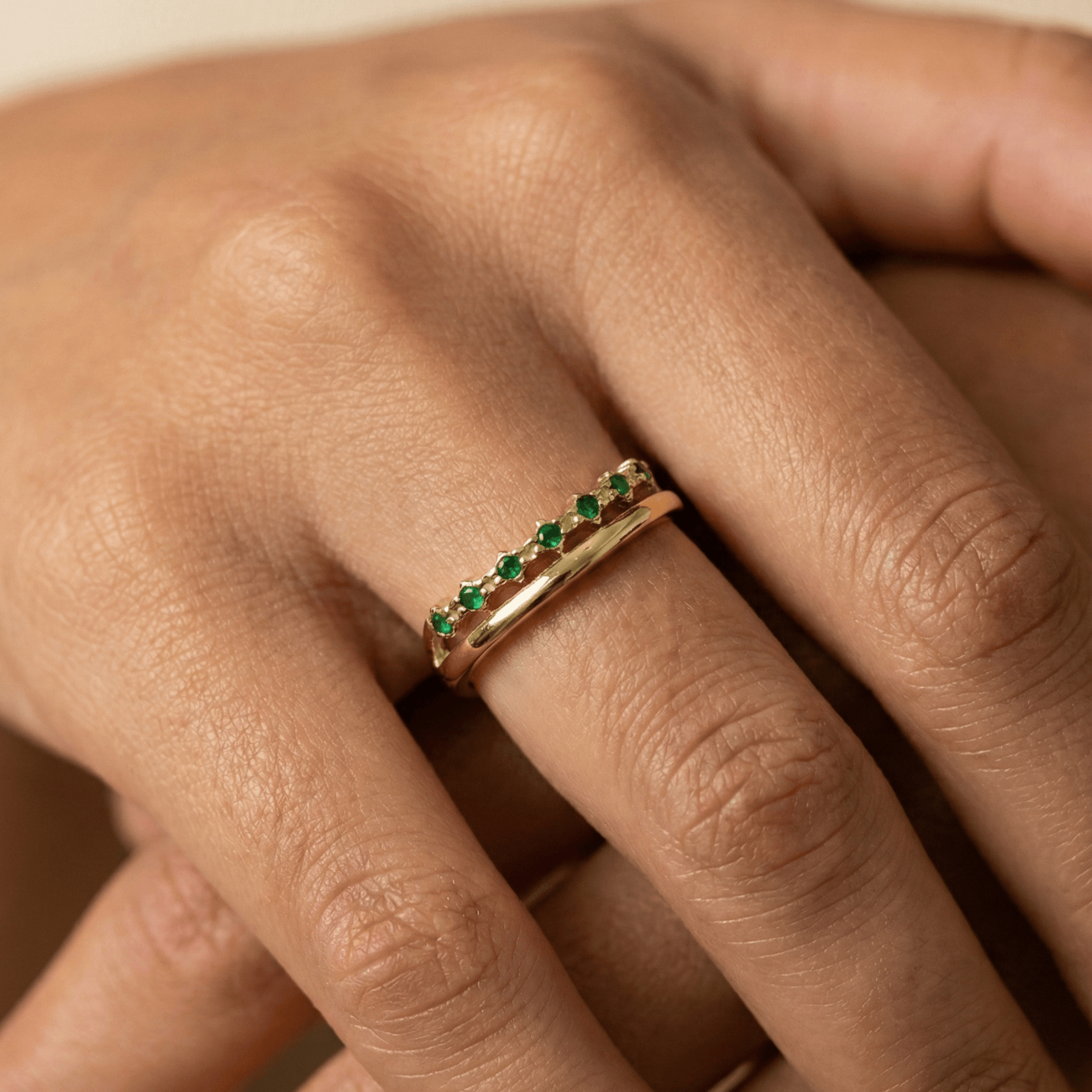 Gold curved stacking ring with emerald green crystals on white pedestal MXW Jewellery