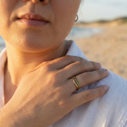 Gold curved stacking ring with emerald green crystals on white pedestal MXW Jewellery