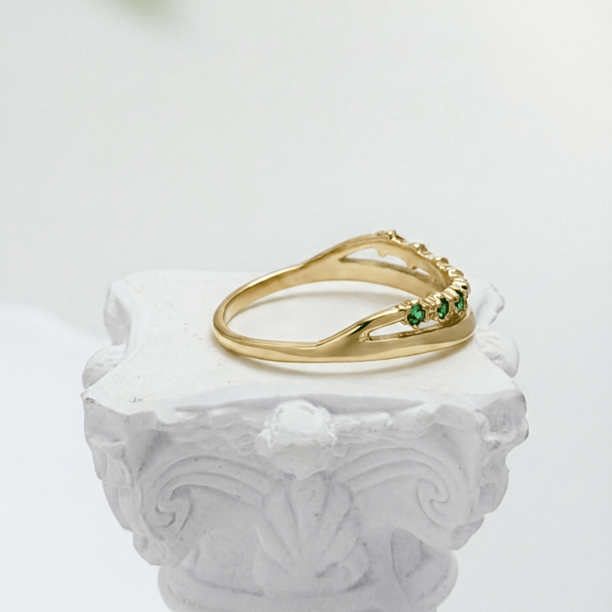 Gold curved stacking ring with emerald green crystals on white pedestal MXW Jewellery