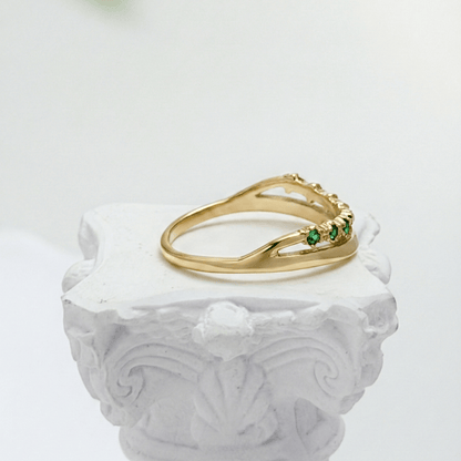 Gold curved stacking ring with emerald green crystals on white pedestal MXW Jewellery
