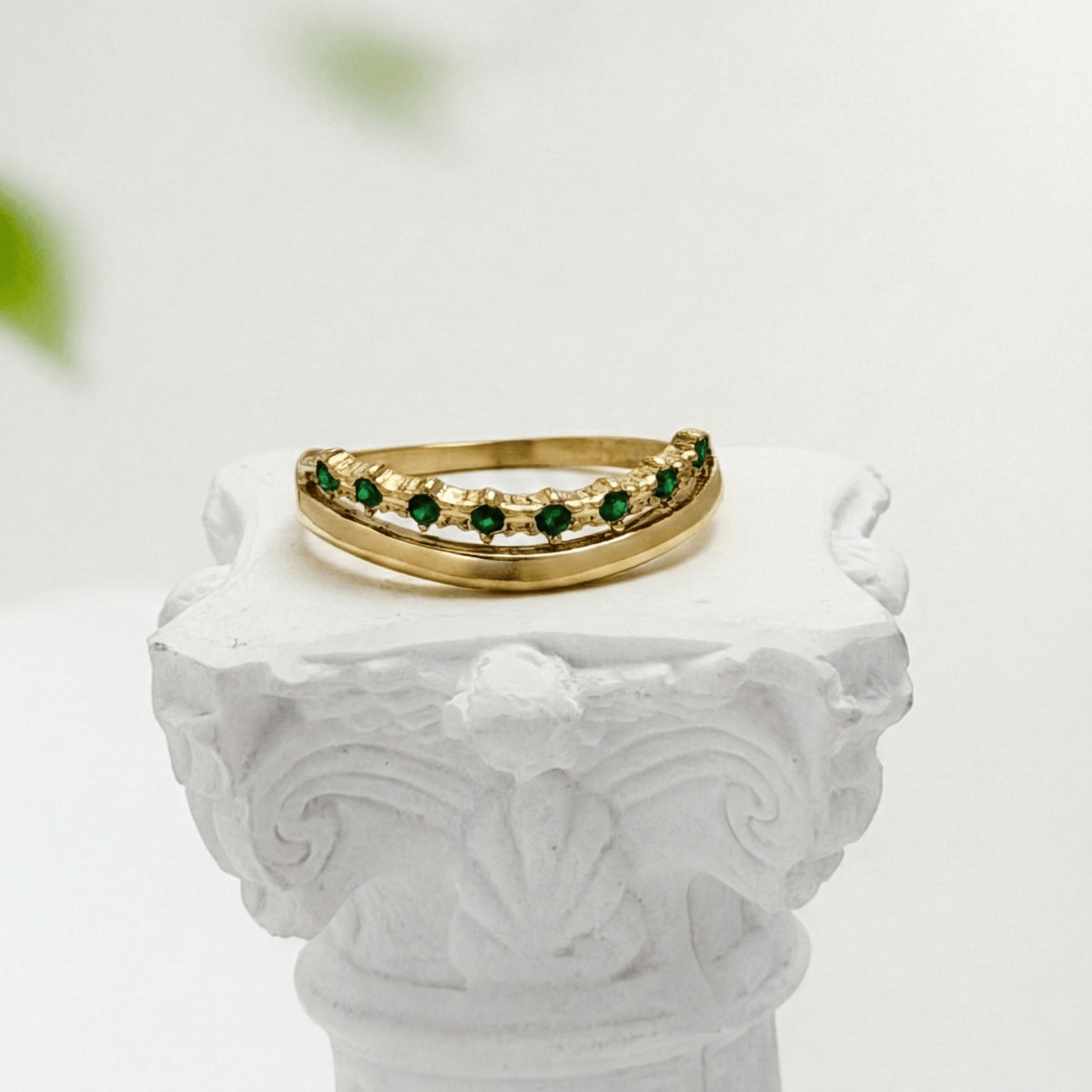 Gold curved stacking ring with emerald green crystals on white pedestal MXW Jewellery
