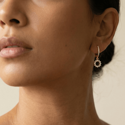 Gold huggie earrings featuring a pave crystal open circle charm dangling from a crystal hoop by MXW Jewellery