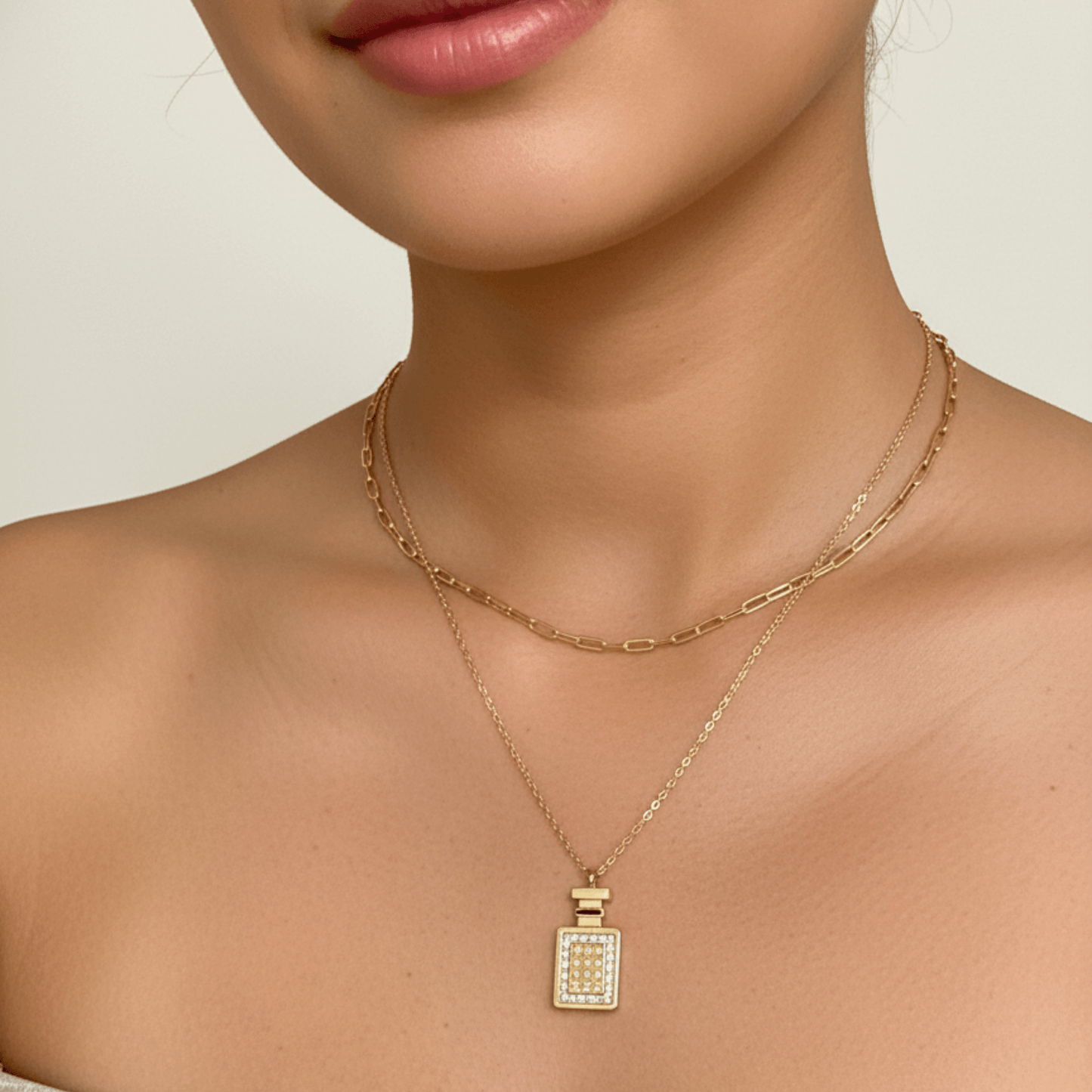 Gold perfume bottle pendant necklace with crystal detailing, symbolising elegance and charm.