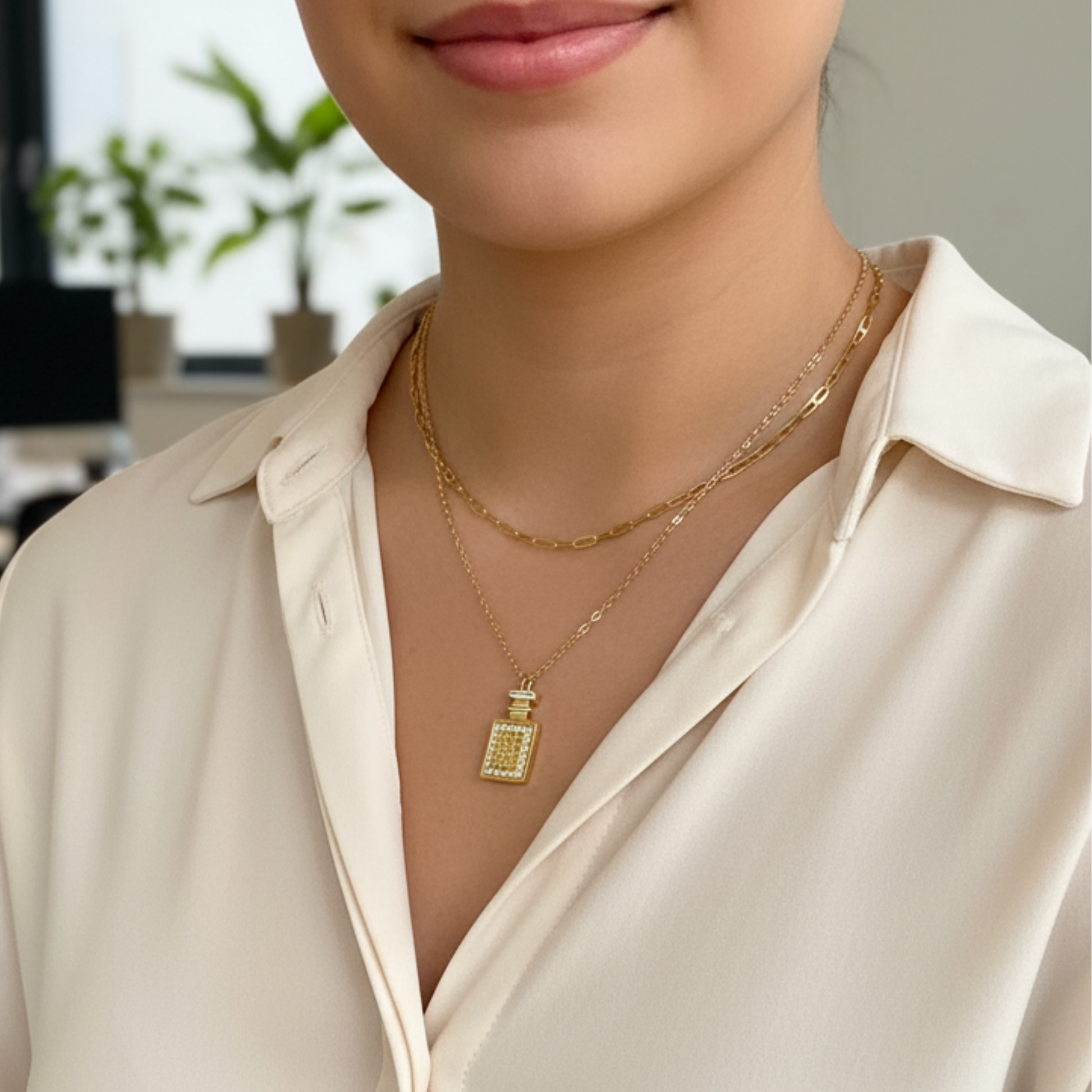 Gold perfume bottle pendant necklace with crystal detailing, symbolising elegance and charm.