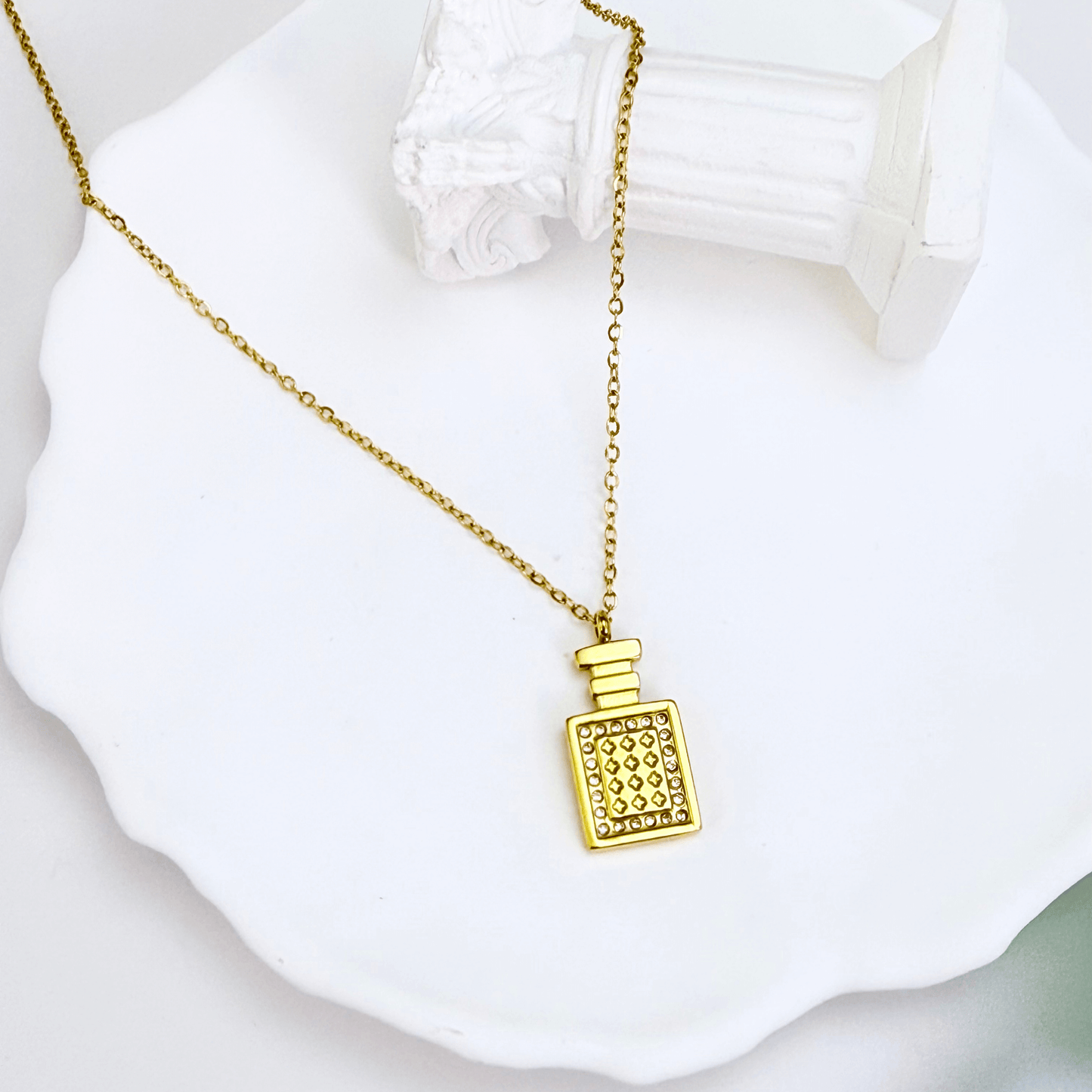 Gold perfume bottle pendant necklace with crystal detailing, symbolising elegance and charm.