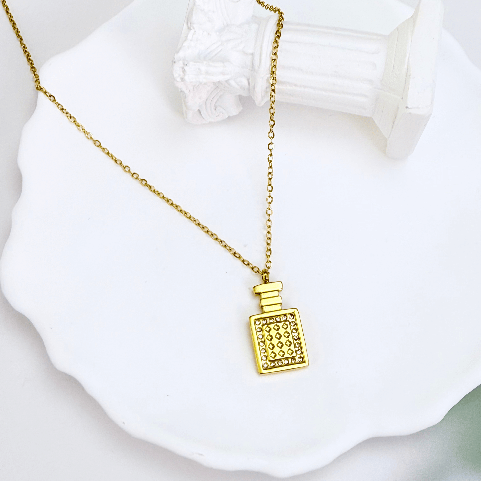 Gold perfume bottle pendant necklace with crystal detailing, symbolising elegance and charm.