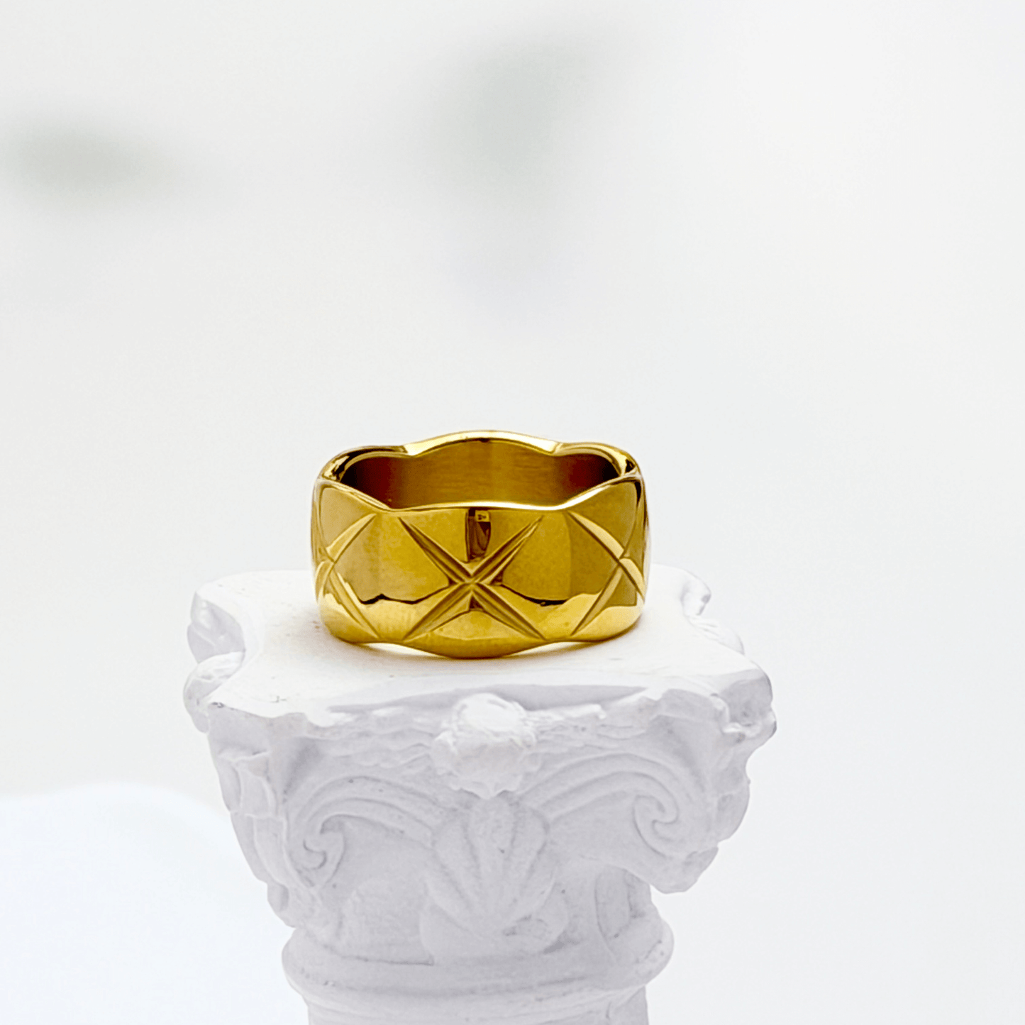 Quilted Gold Band Ring by MXW Jewellery, featuring a wide gold band with a geometric cross-hatch pattern on a white pedestal.
