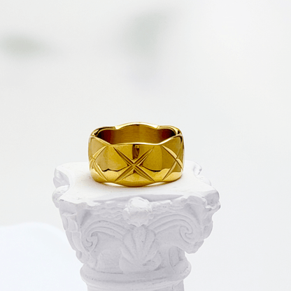 Quilted Gold Band Ring by MXW Jewellery, featuring a wide gold band with a geometric cross-hatch pattern on a white pedestal.