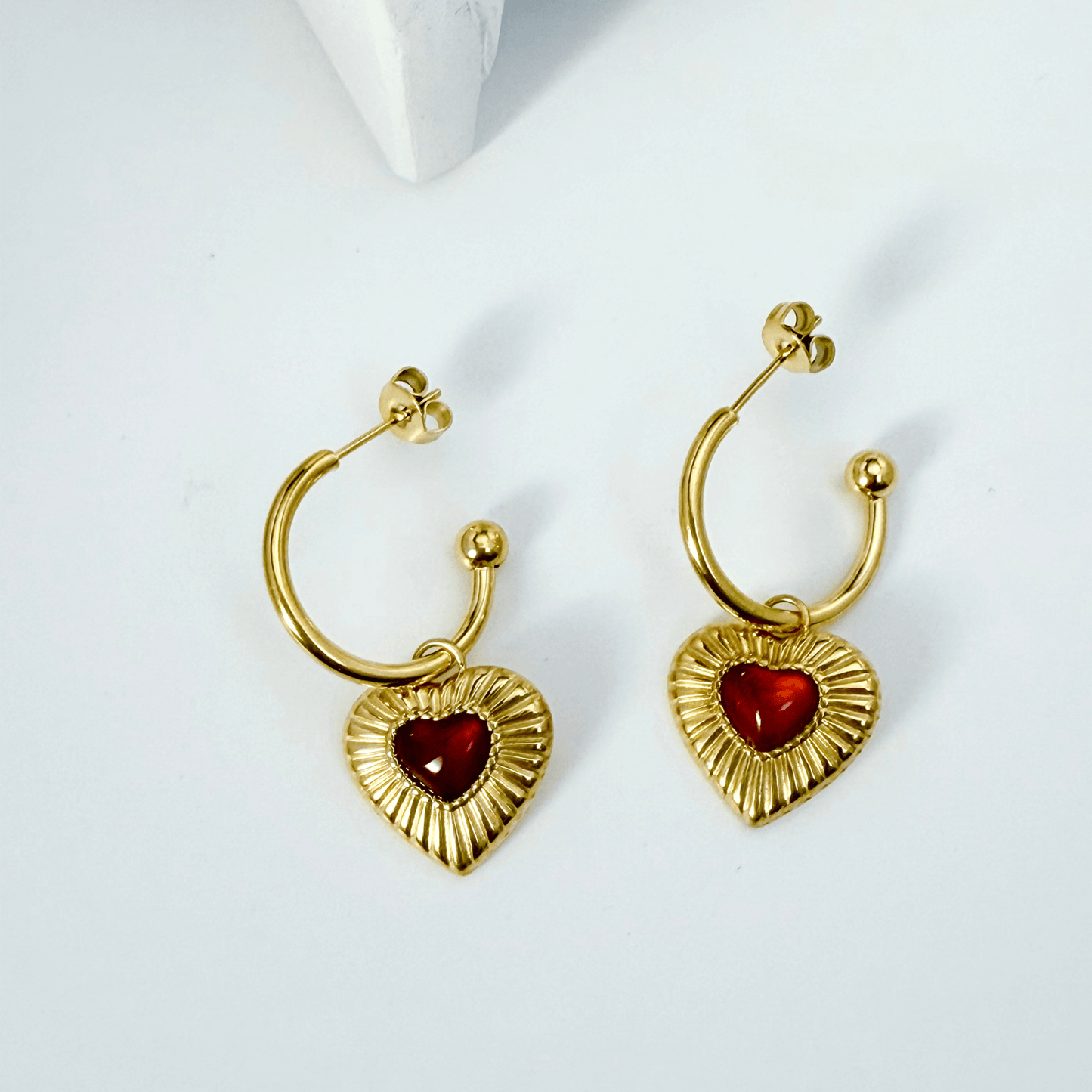 Gold hoop earrings featuring a textured heart charm with a red agate stone centre