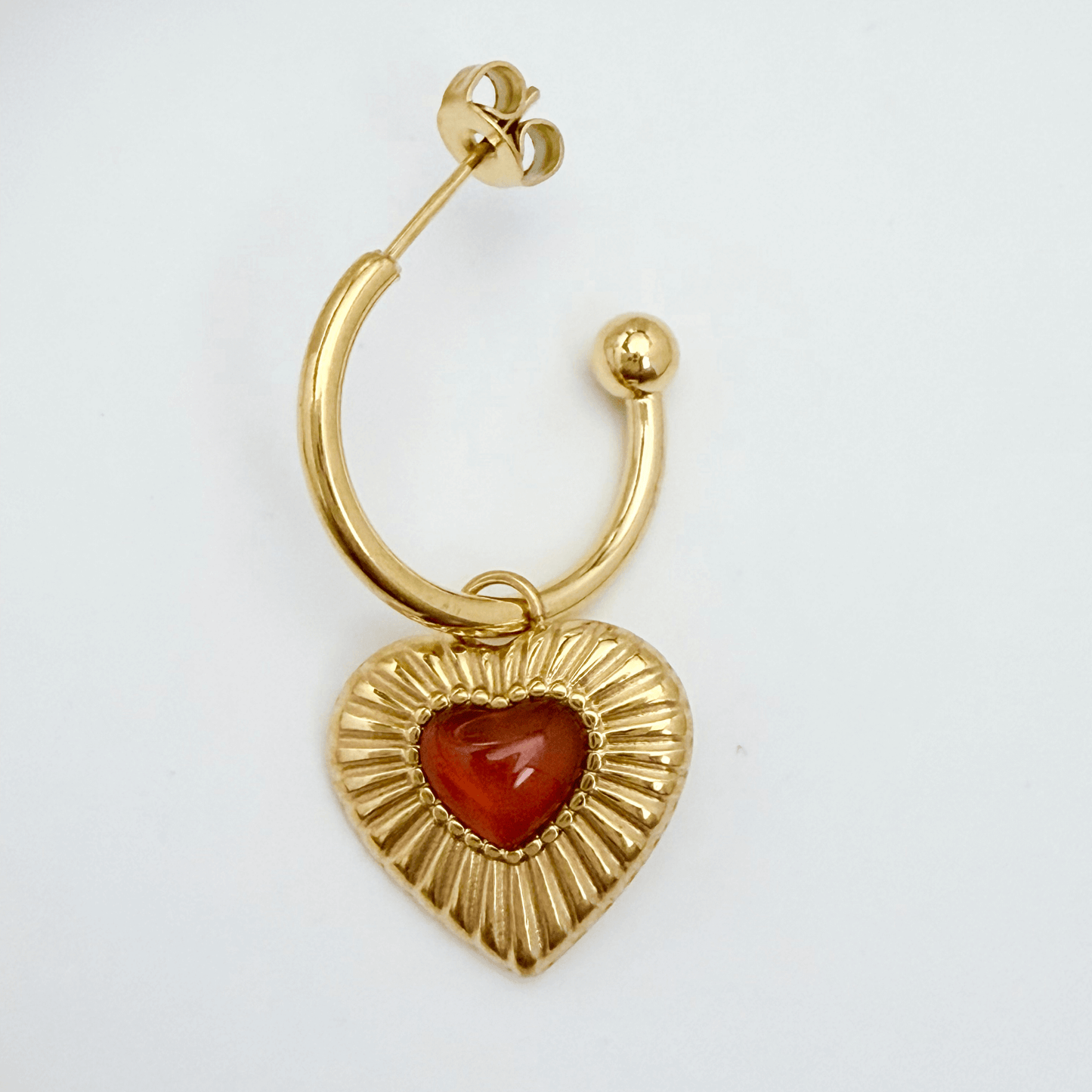 Gold hoop earrings featuring a textured heart charm with a red agate stone centre