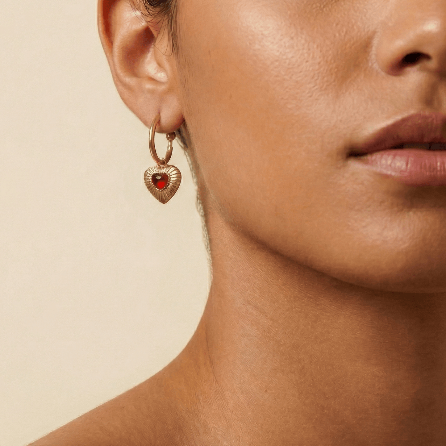 Gold hoop earrings featuring a textured heart charm with a red agate stone centre