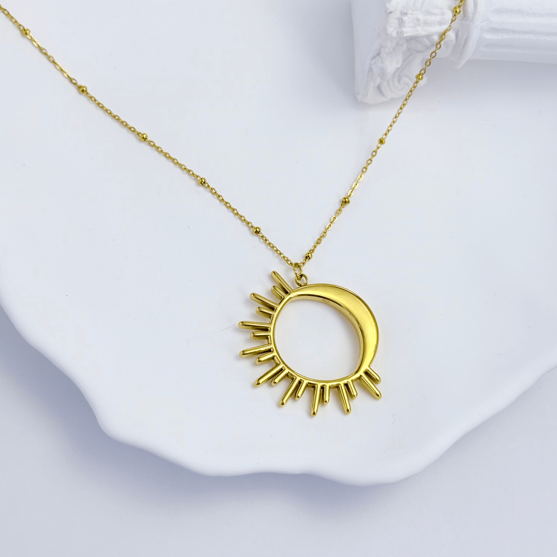 Waterproof gold solar eclipse necklace featuring a crescent moon overlapping a radiant sunburst design on a fine beaded chain, made with PVD gold plated stainless steel.
