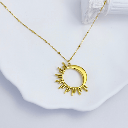 Waterproof gold solar eclipse necklace featuring a crescent moon overlapping a radiant sunburst design on a fine beaded chain, made with PVD gold plated stainless steel.