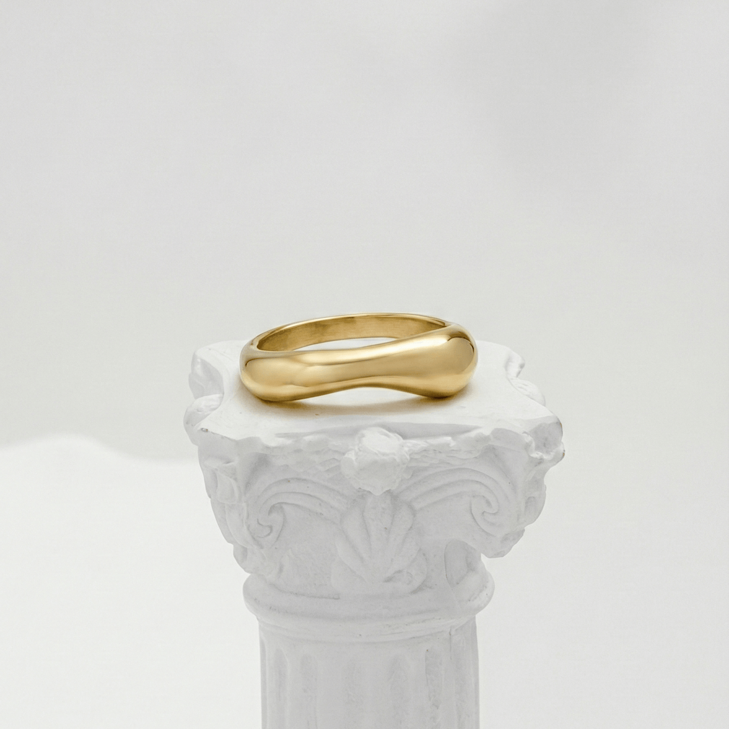 Gold Wave Ring by MXW Jewellery featuring a sculptural fluid design and waterproof gold finish displayed on a white textured column