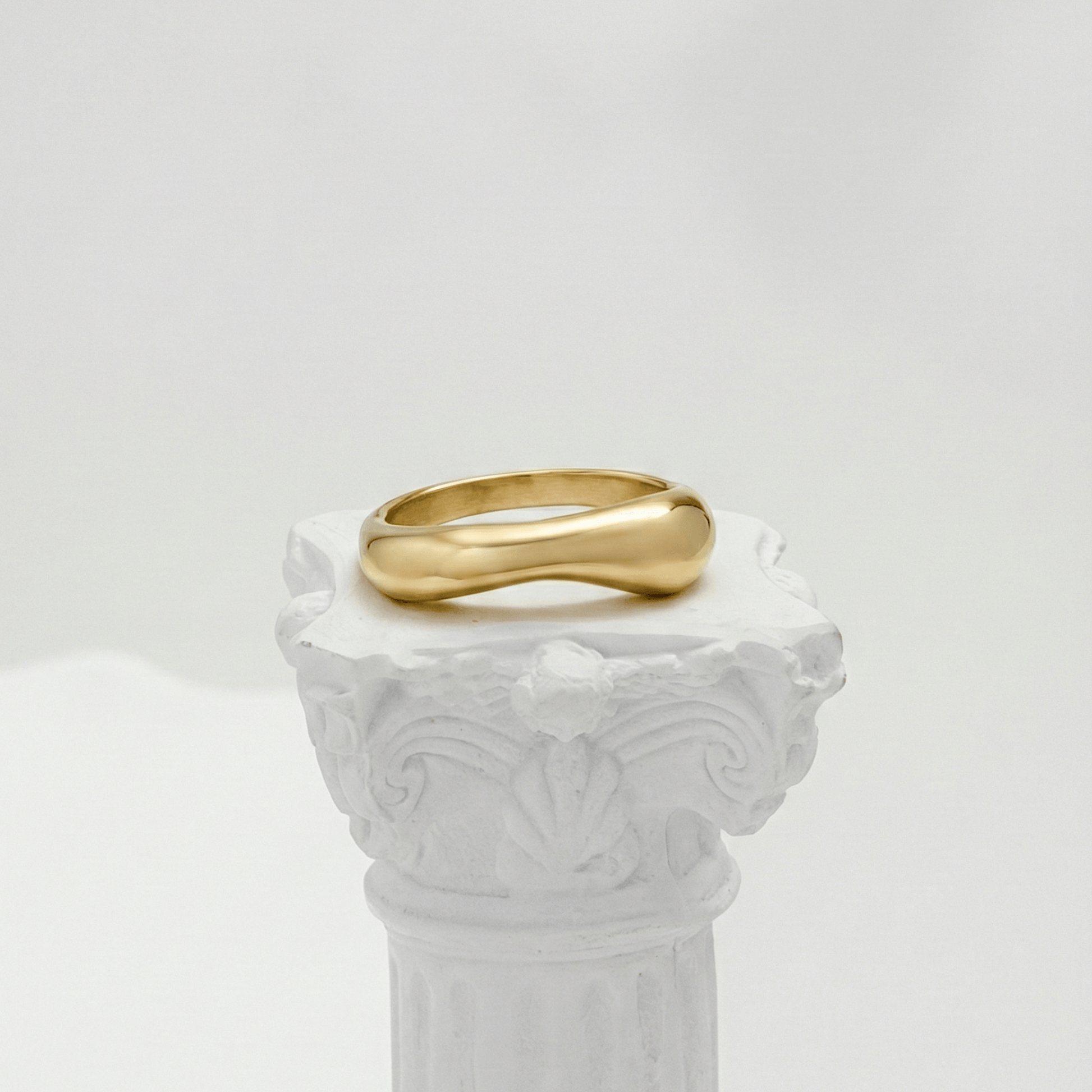 Gold Wave Ring by MXW Jewellery featuring a sculptural fluid design and waterproof gold finish displayed on a white textured column