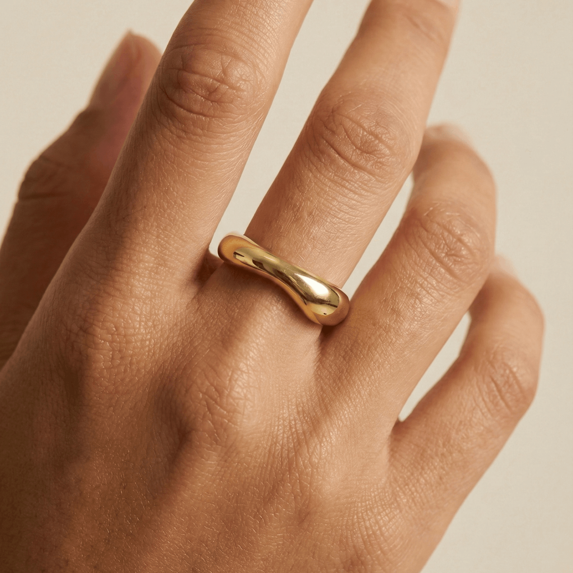 Gold Wave Ring by MXW Jewellery featuring a sculptural fluid design and waterproof gold finish displayed on a white textured column