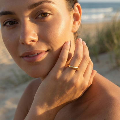 Gold Wave Ring by MXW Jewellery featuring a sculptural fluid design and waterproof gold finish displayed on a white textured column