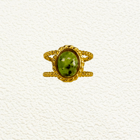 Adjustable gold PVD ring featuring a green natural stone with double beaded band, styled on white scallop dish with soft floral background.