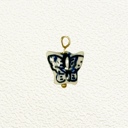 Blue and white ceramic butterfly charm with abstract wing patterns and gold loop