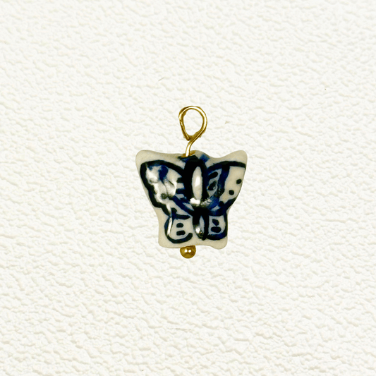 Blue and white ceramic butterfly charm with abstract wing patterns and gold loop