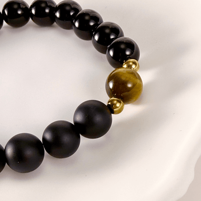 Men’s bracelet with polished black agate beads, single tiger’s eye gemstone, and gold accents on stretch cord.