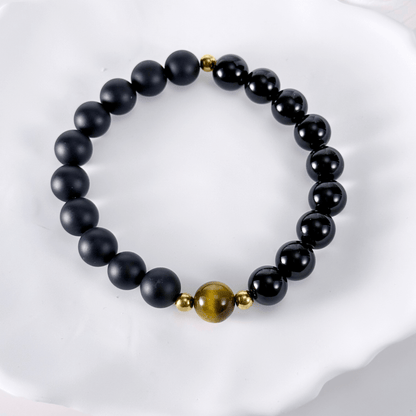 Men’s bracelet with polished black agate beads, single tiger’s eye gemstone, and gold accents on stretch cord.