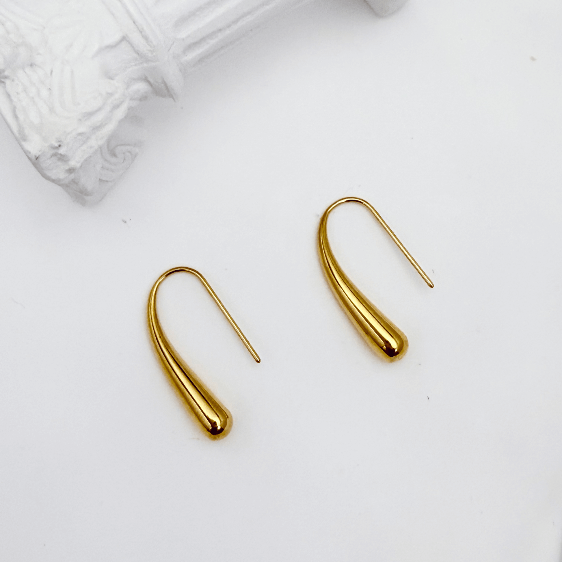 Pair of polished gold tapered raindrop earrings with elongated hook design on white background.