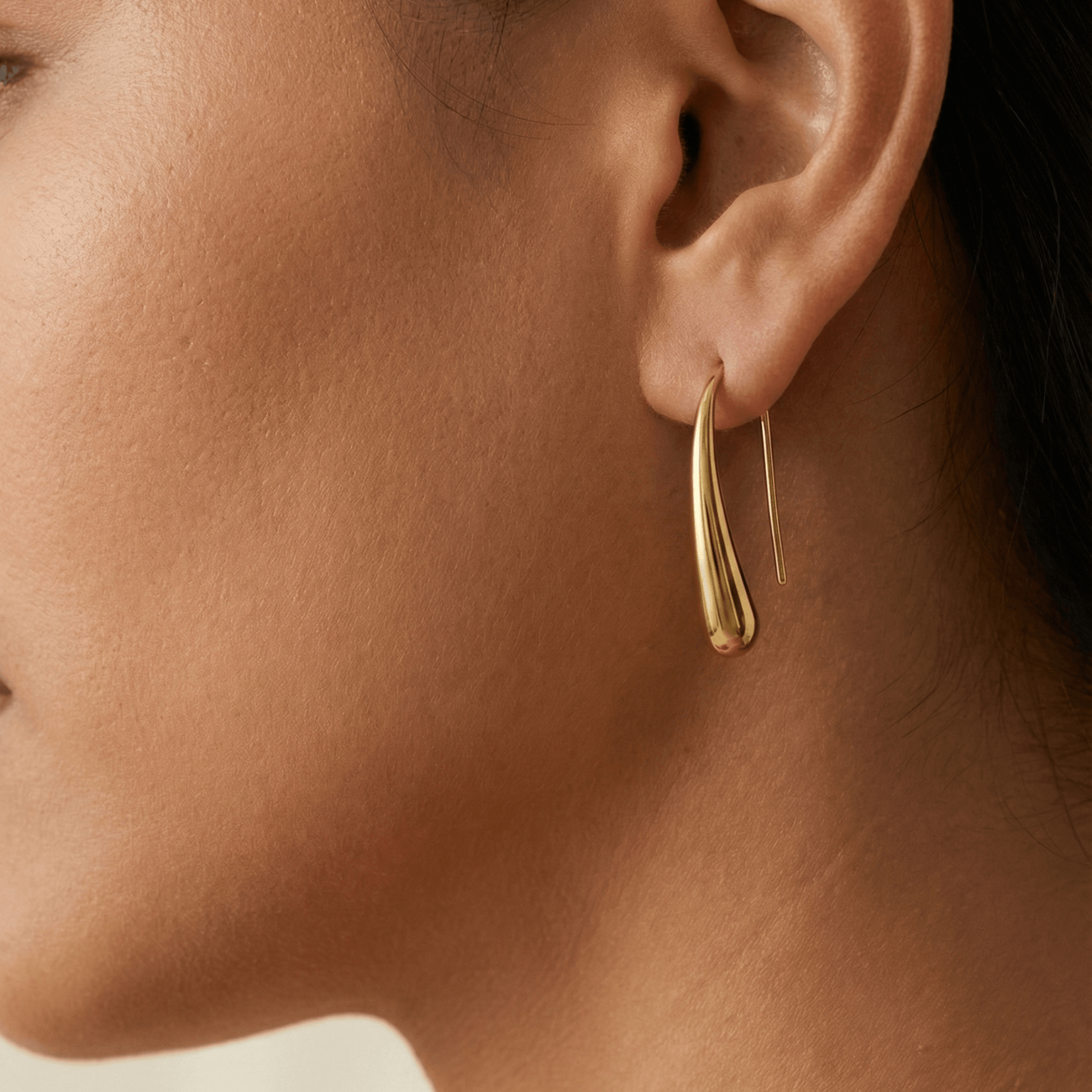 Pair of polished gold tapered raindrop earrings with elongated hook design on white background.